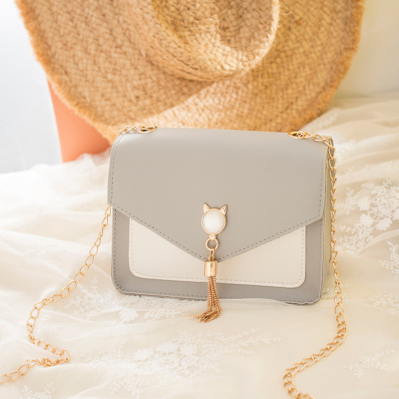 Light gray small messenger bag with cat charm, tassel drop, and gold chain strap
