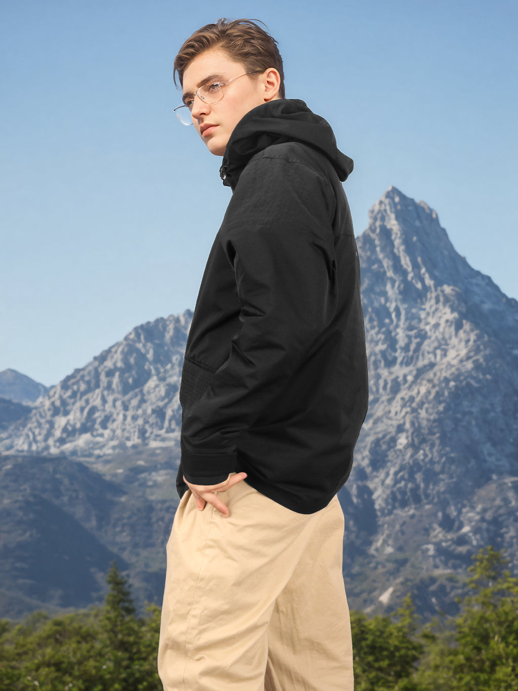 Black hooded rain jacket side view on model outdoors with snap front and hood